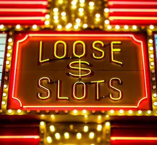 Bright neon lights display the words 'Loose Slots' with a dollar sign in the center. The sign is outlined with bulbs, creating a vibrant and flashy effect typical of a casino or entertainment venue.